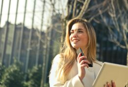 Smiling businesswoman holding smartphone and tablet outdoors in Milan.